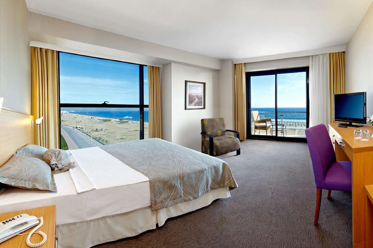A hotel room with a bed, a desk, a chair, a TV, and a view of the ocean.