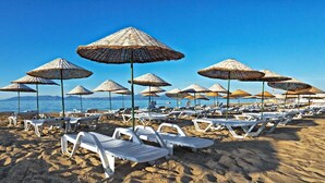 A beach with rows of white lounge chairs and thatched umbrellas. - Ayvalik Cinar Hotel (Ayvalik)