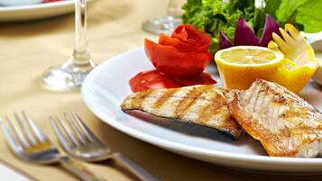 Une table à manger avec une assiette de poisson grillé, une salade et deux verres de vin blanc.