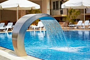 Una piscina al aire libre, sombrillas, sillones reclinables de piscina