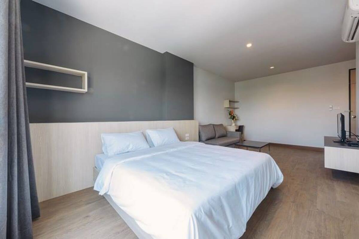 A modern hotel room with a large bed, a bedside table, a small sofa, and a TV.