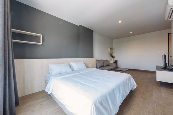 A modern hotel room with a large bed, a bedside table, a small sofa, and a TV. - MT Park Residence (Chonburi)