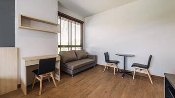 A modern room with a wooden desk, a grey sofa, two black chairs, and a small round table.