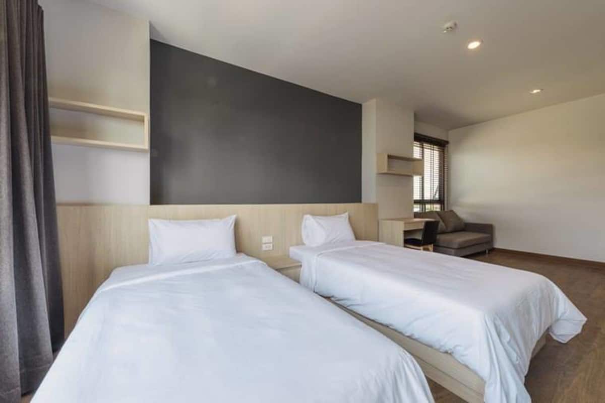 A hotel room with two single beds, a desk, a chair, and a large window.