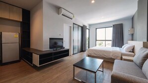 A modern hotel room with a kitchenette, a flat-screen TV, a bed, a sofa, and a large window offering a view. - MT Park Residence (Chonburi)