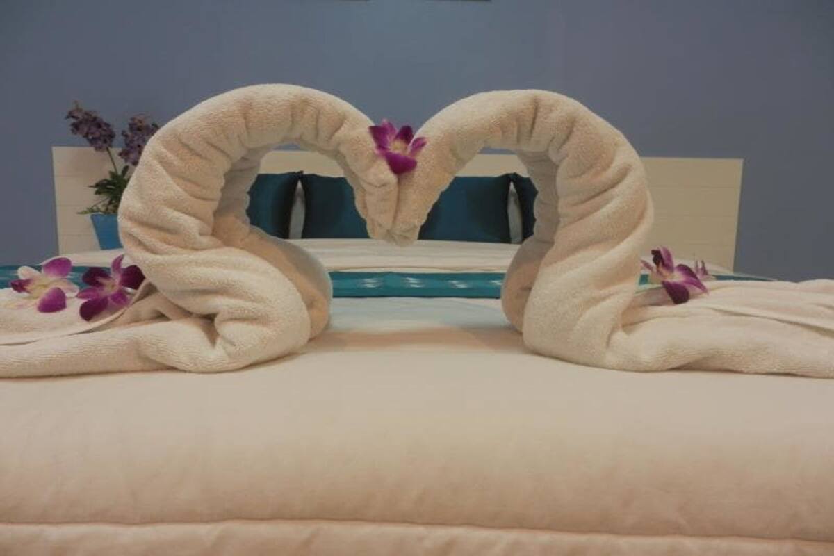 A bed with a heart-shaped towel arrangement and purple flowers.