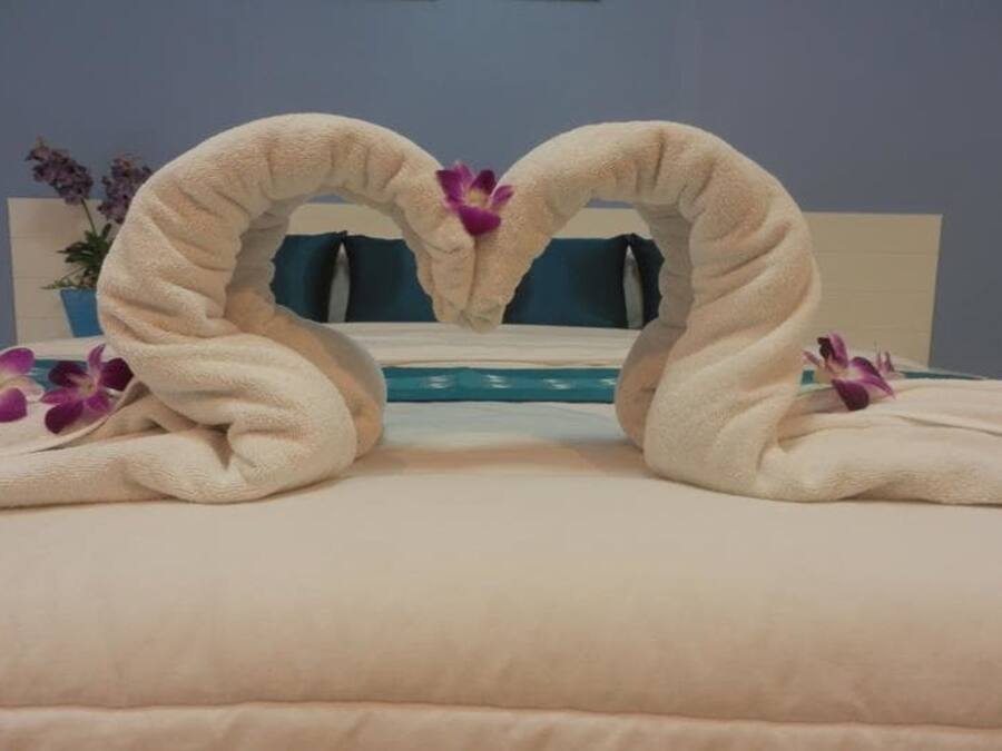 A bed with a heart-shaped towel arrangement and purple flowers.