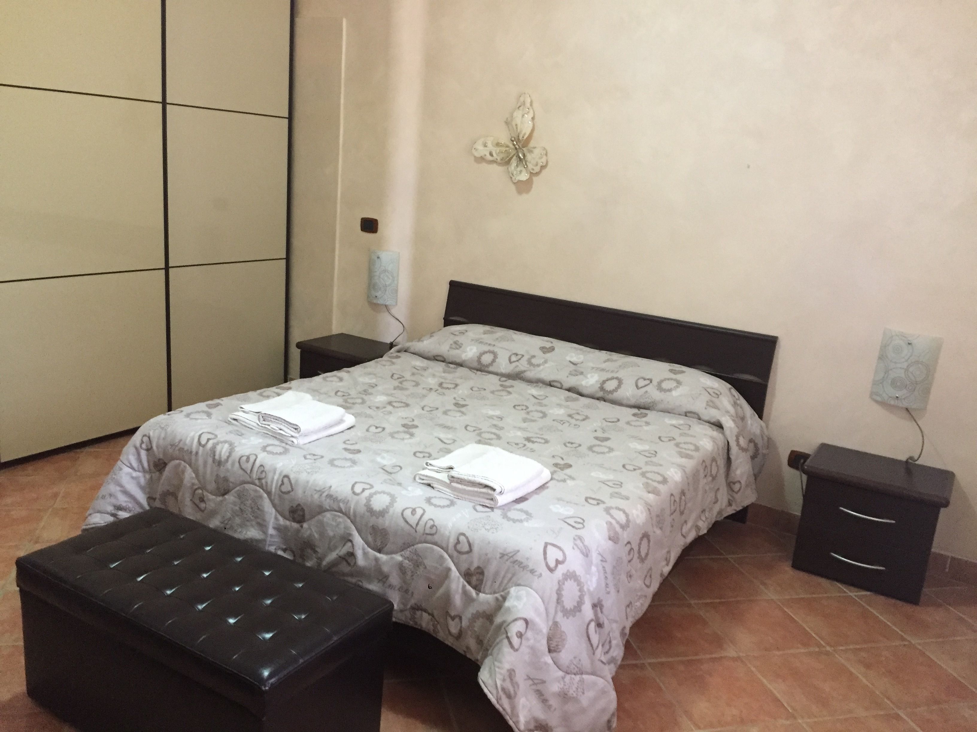 Quarto com cama, mesa de cabeceira, cômoda e uma borboleta decorativa na parede.