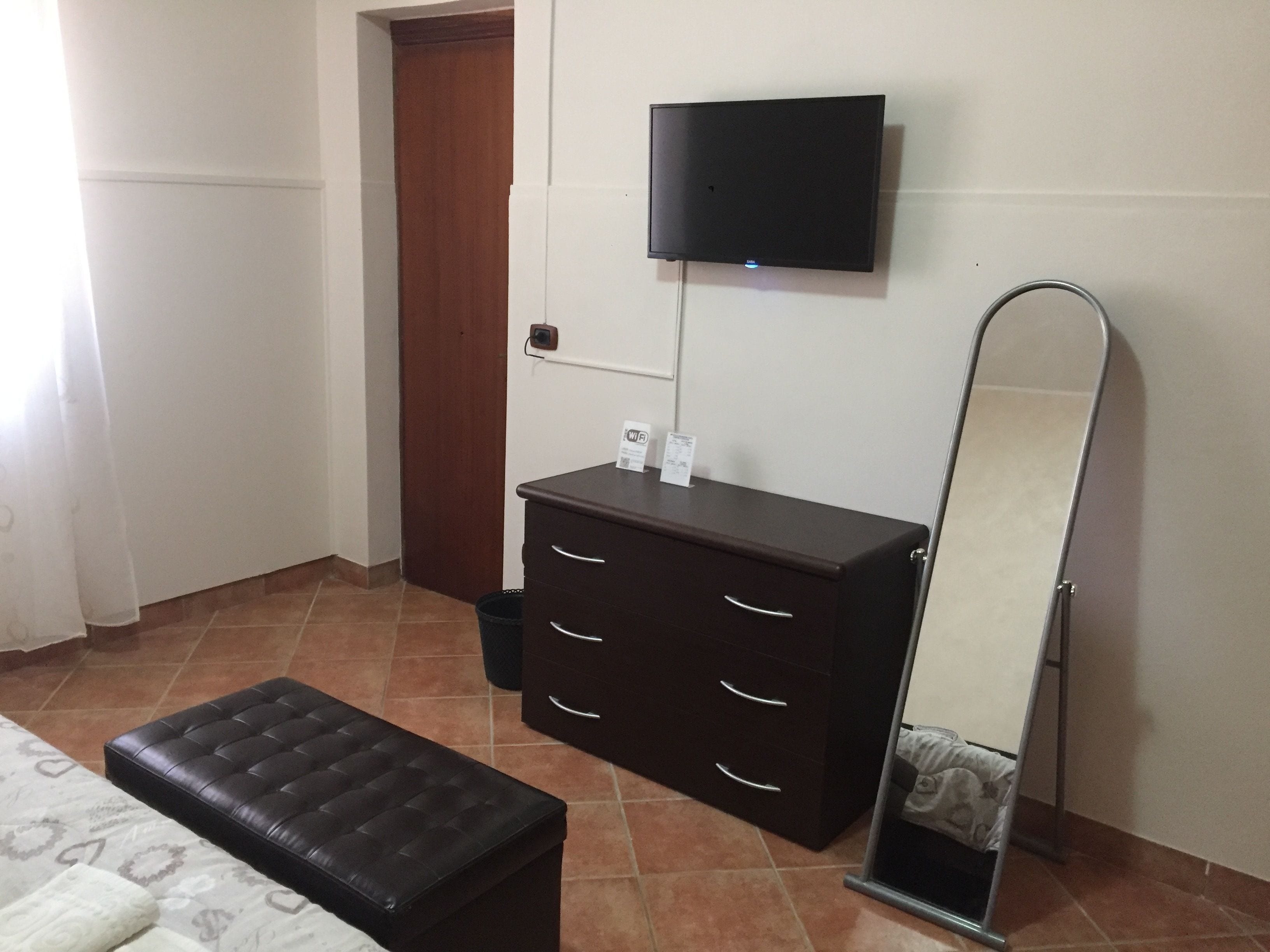 A bedroom with a bed, a dresser, a television mounted on the wall, and a mirror.