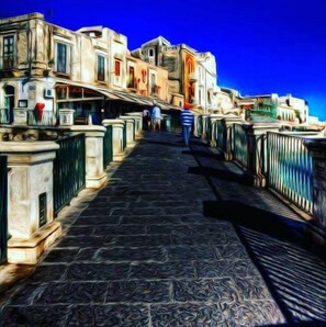 A stone pathway leading to a row of buildings with balconies, under a clear blue sky.