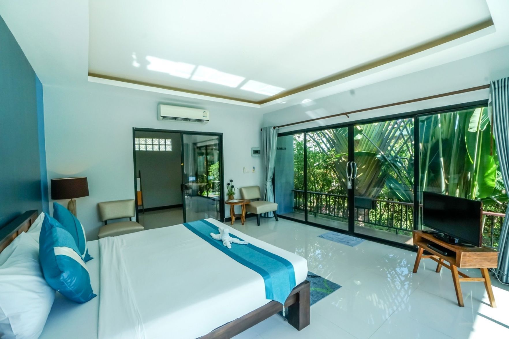 Habitación de hotel con cama, televisión, escritorio y balcón con vistas a la vegetación.