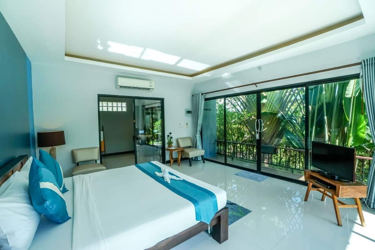 Habitación de hotel con cama, televisión, escritorio y balcón con vistas a la vegetación.