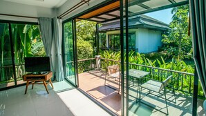 Una habitación moderna con amplios ventanales que dan a un balcón con vistas a exuberante vegetación y una casa.