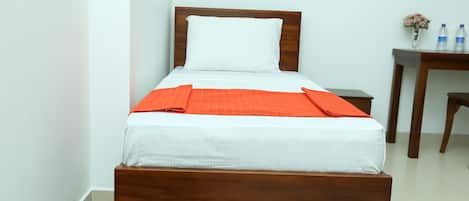 A neatly made bed with a wooden headboard and white bedding, a small wooden nightstand with a vase of flowers, and a chair in a hotel room.