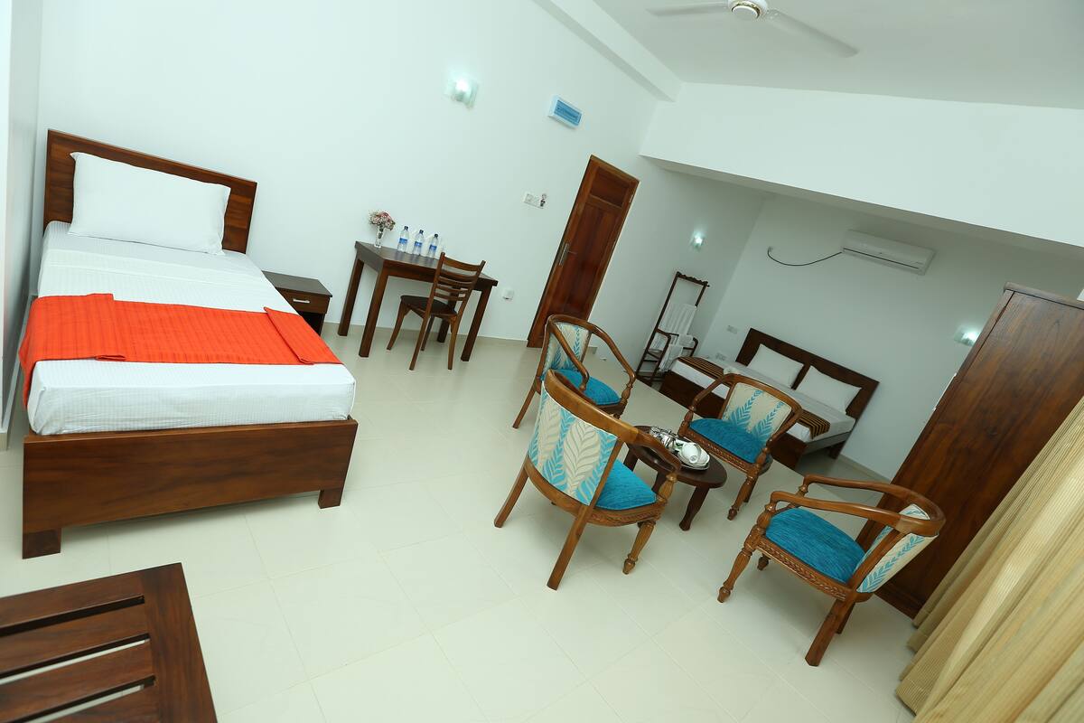 Une chambre d’hôtel avec un lit, deux chaises en bois, une petite table avec des bouteilles d’eau et un bureau avec une chaise.