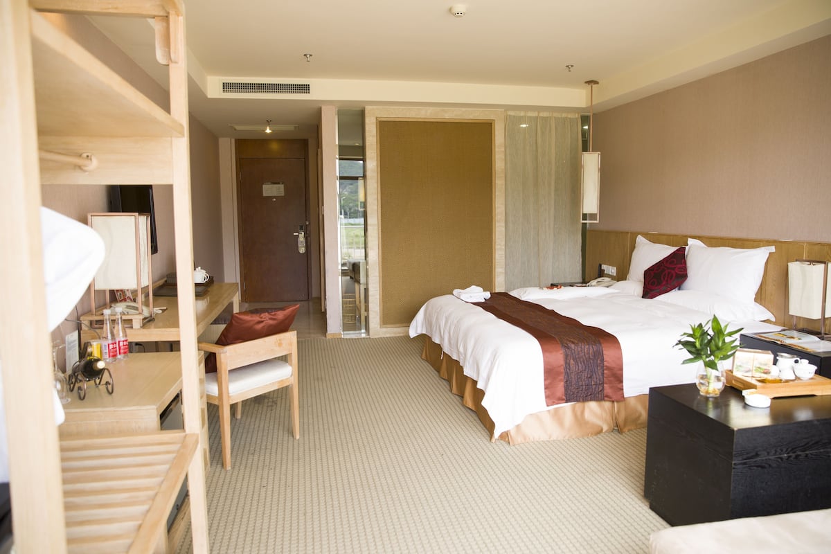A hotel room with a bed, desk, chair, and a small table with a plant and tray.
