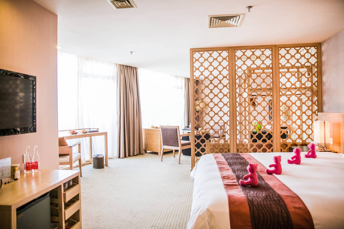 A hotel room with a bed, a desk, a chair, a TV, and a large window with curtains.