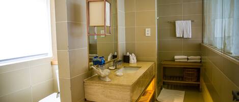 A modern bathroom with a beige tiled wall, a wooden vanity, a large mirror, and a window with curtains.