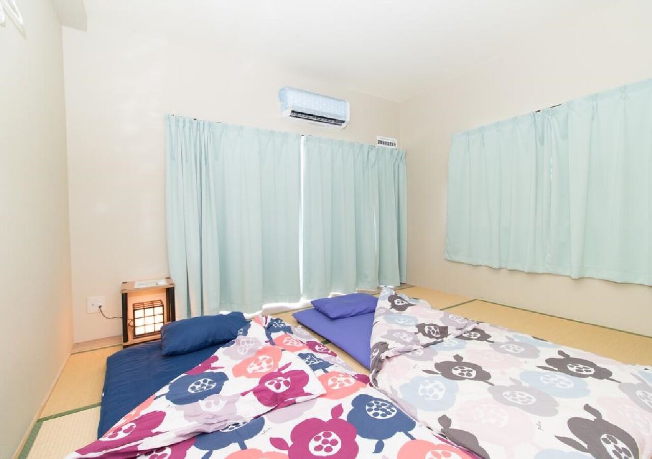 Ein Zimmer mit zwei Betten, einer Heizung und leichten Vorhängen.