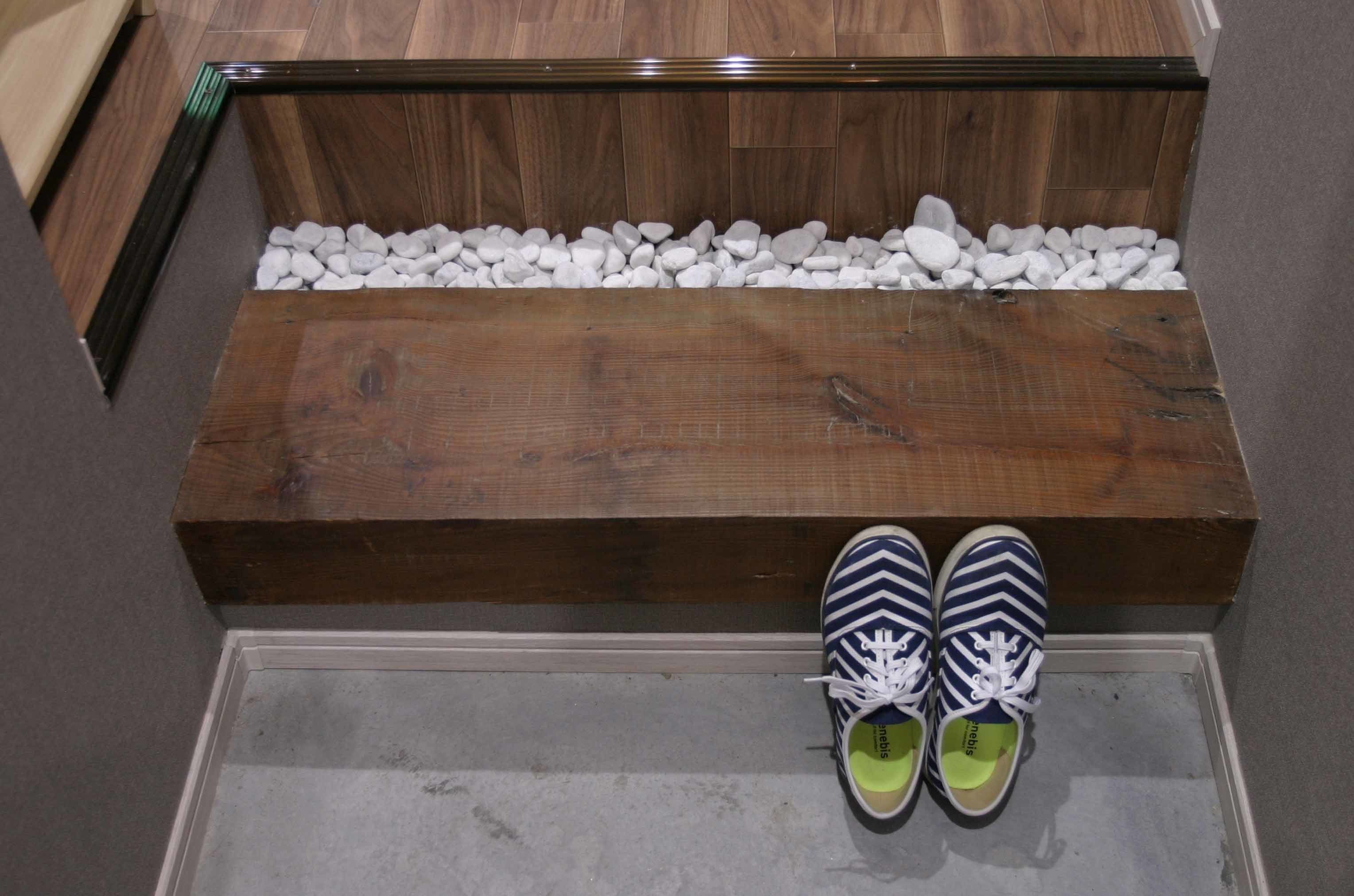 Un banc en bois, recouvert de petits galets blancs, et une paire de chaussures à rayures posée dessus.