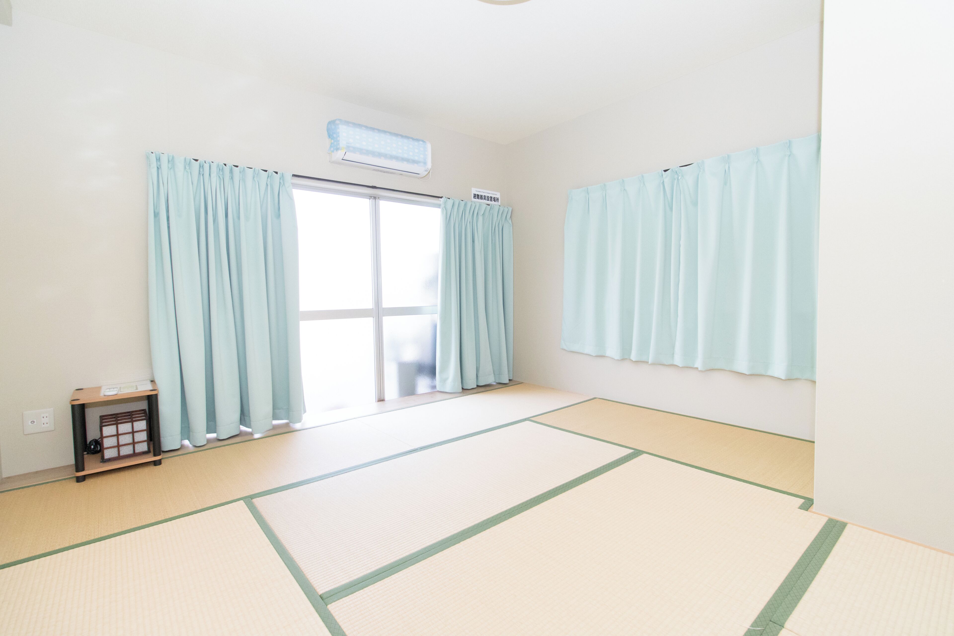 Una habitación con suelo de tatami, puerta corredera y cortinas azul claro.