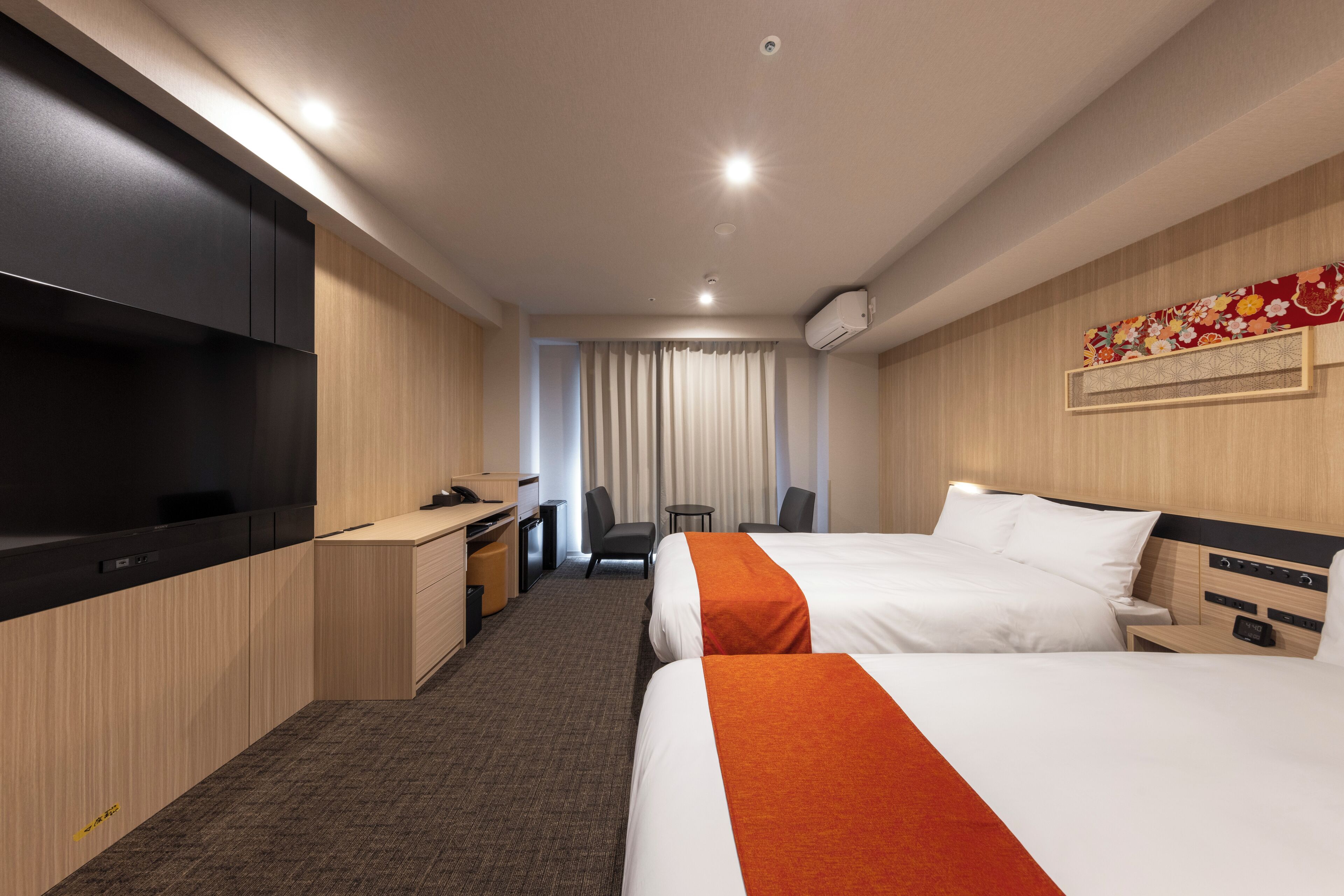 Quarto de hotel com duas camas, uma escrivaninha, uma cadeira, uma televisão e uma cortina.