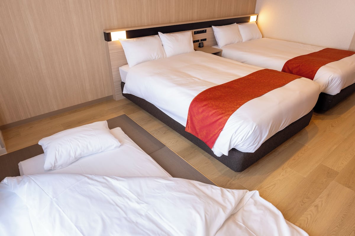 Una habitación de hotel con dos camas, suelo de madera y una mesita de noche con lámpara.