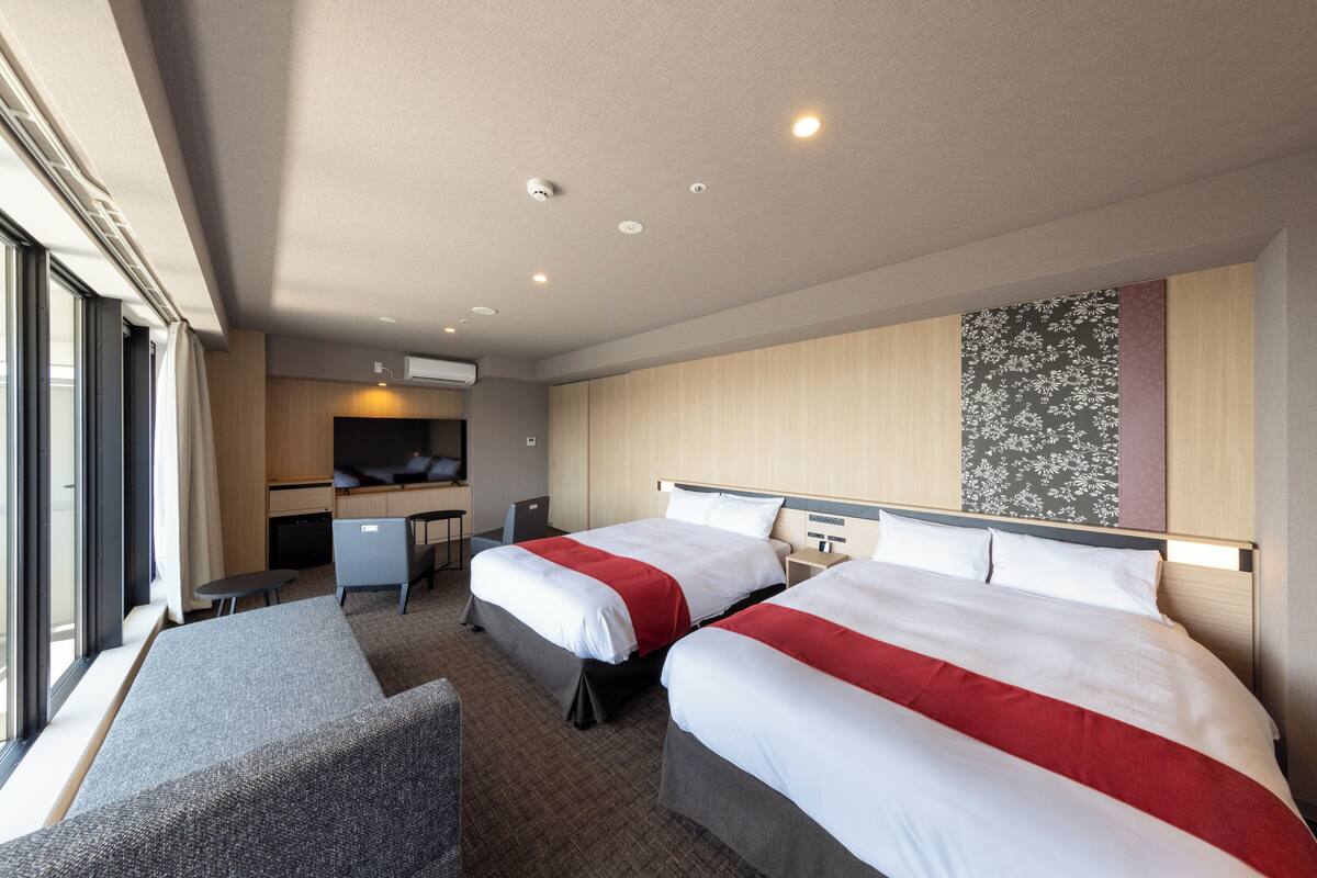 Una habitación de hotel con dos camas, un escritorio, una silla y un ventanal grande.