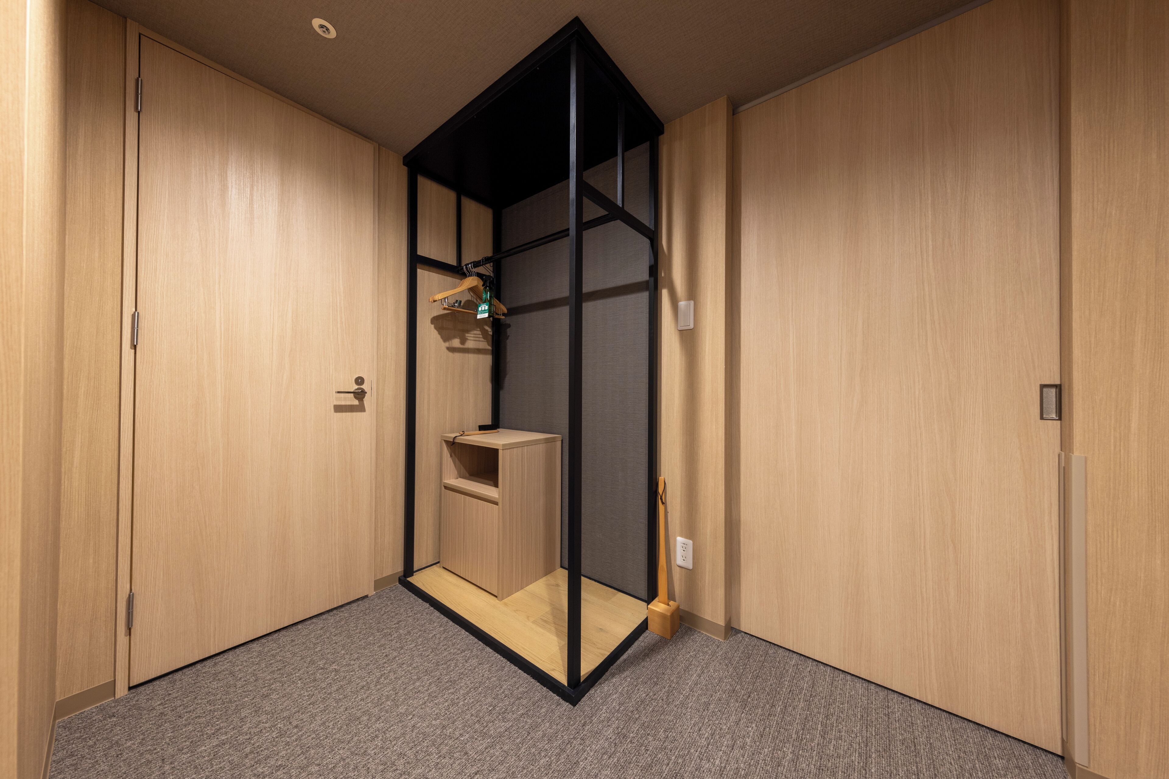 A room with a wooden wardrobe, a small wooden cabinet, and a grey carpet.