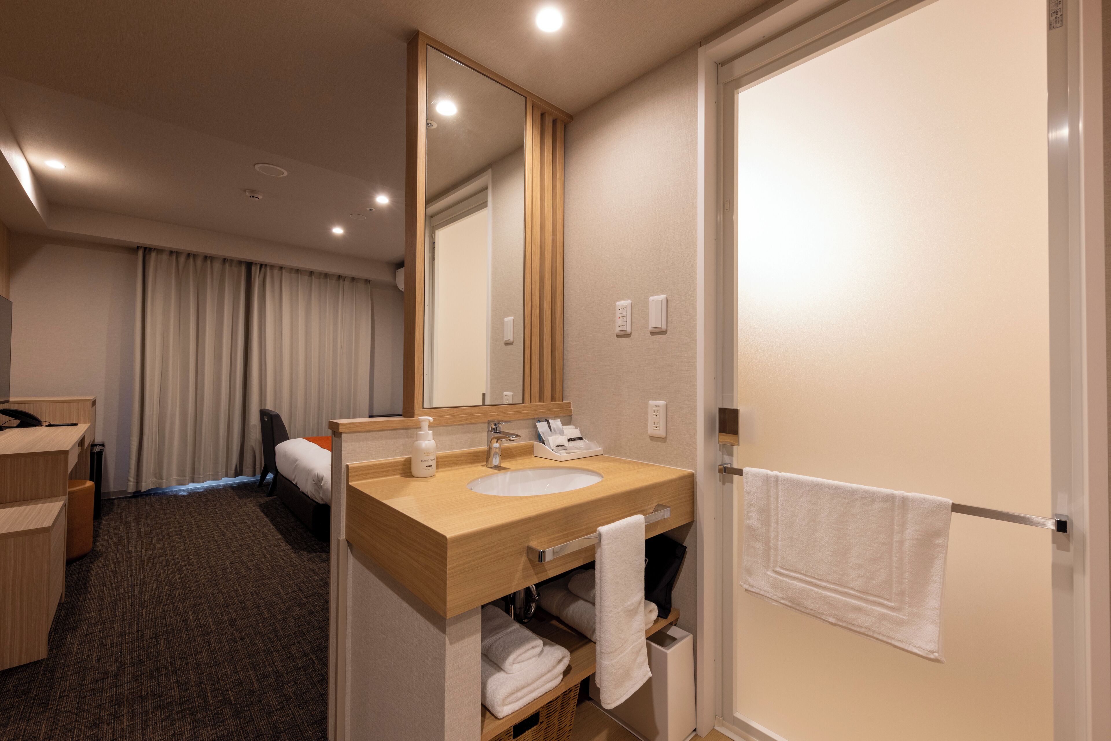 A hotel bathroom with a wooden vanity, a large mirror, a sink, a towel rack, and a door.