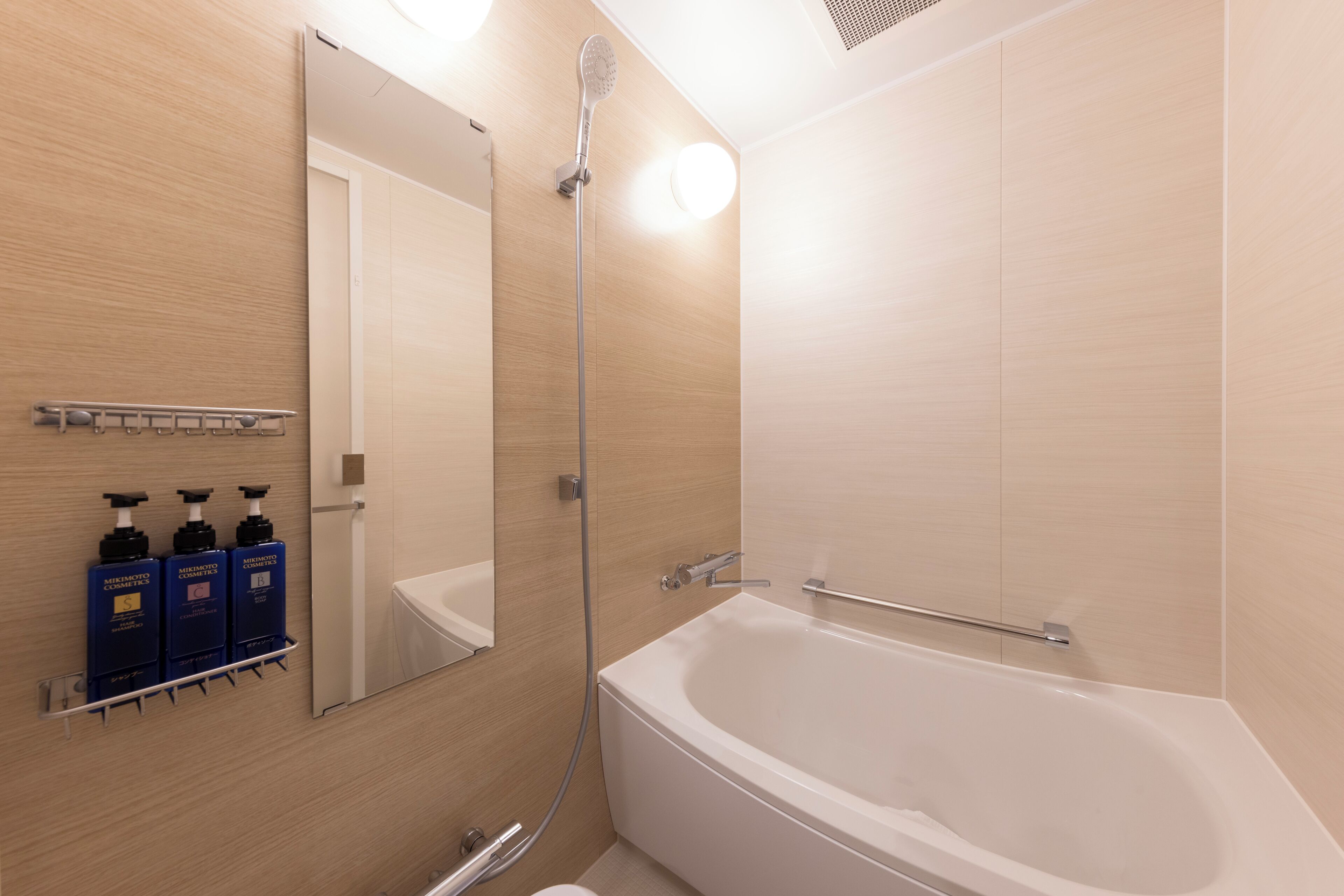 A modern bathroom with a bathtub, a shower, and a mirror. There are three bottles of shampoo and conditioner on a shelf.