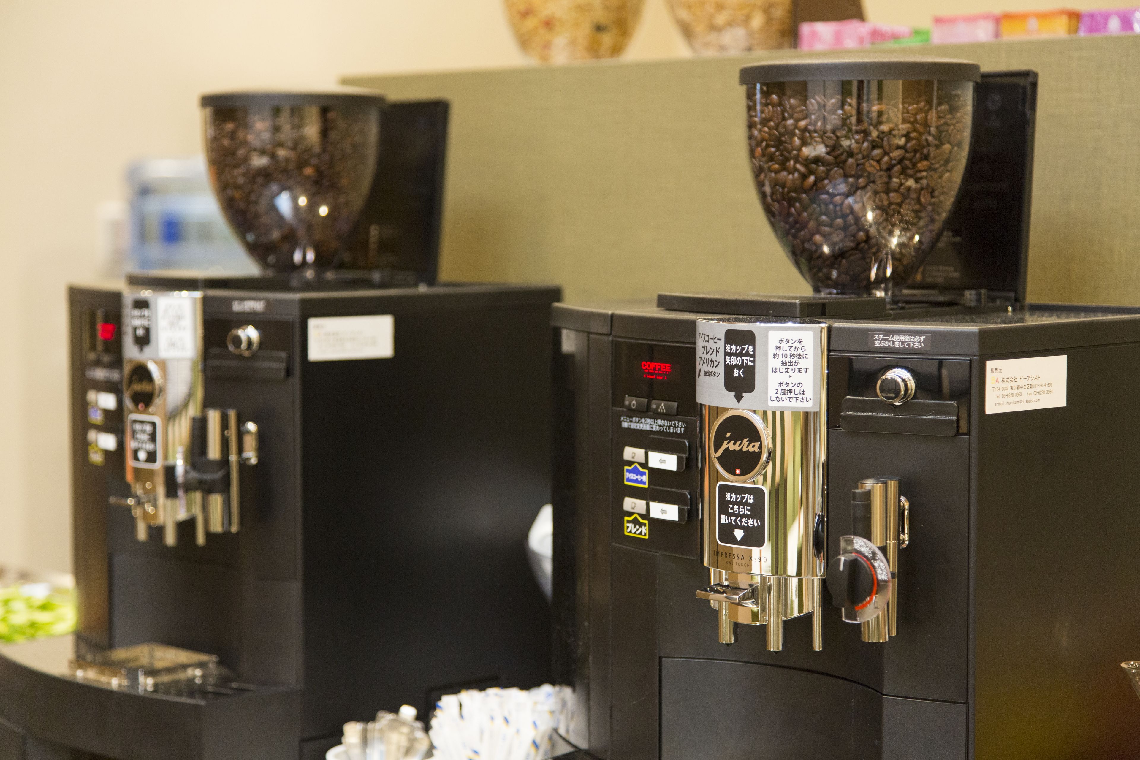 Deux machines à café avec des grains de café dans des récipients transparents, un distributeur d’eau et une étiquette pour le café.