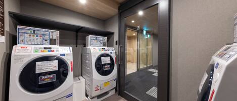 A laundry area with two washing machines and a dryer, a wooden ceiling, and a glass door leading to another room.