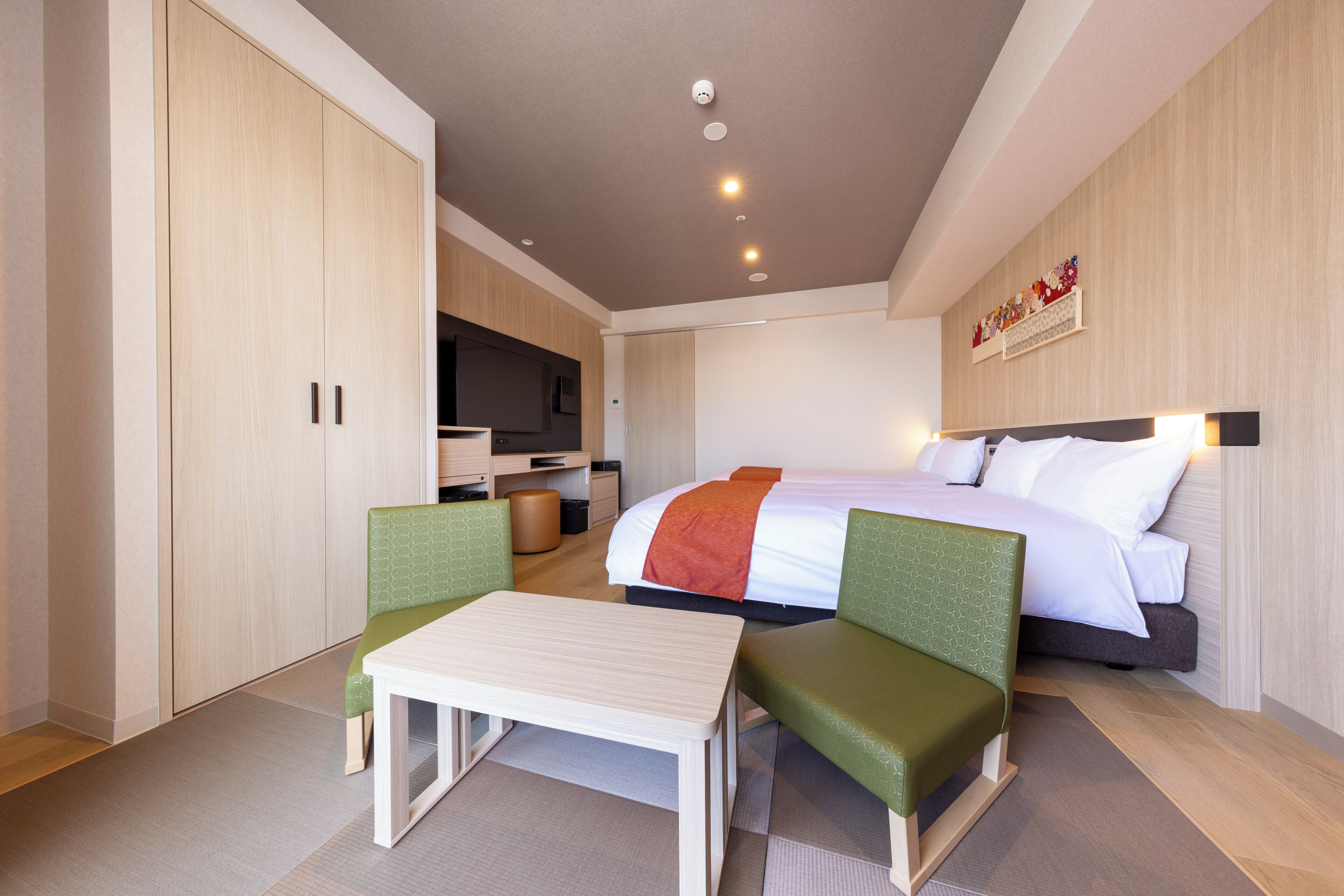 A hotel room with a bed, a desk, two chairs, a television, and a wardrobe.