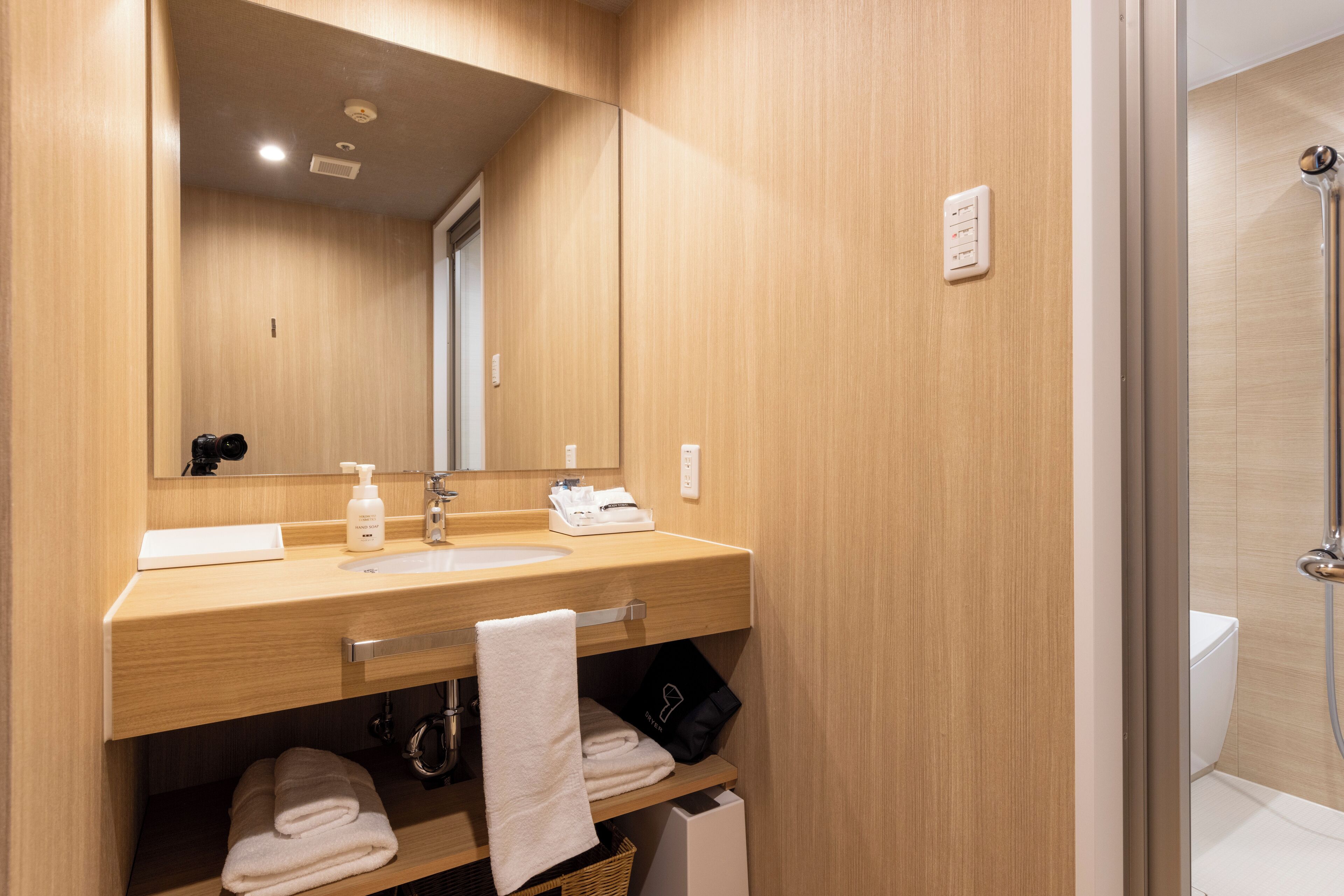 A modern bathroom with a wooden vanity, a large mirror, a shower area, and neatly folded towels.