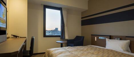 A hotel room with a bed, a desk, a chair, a small table, and a window with a city view.