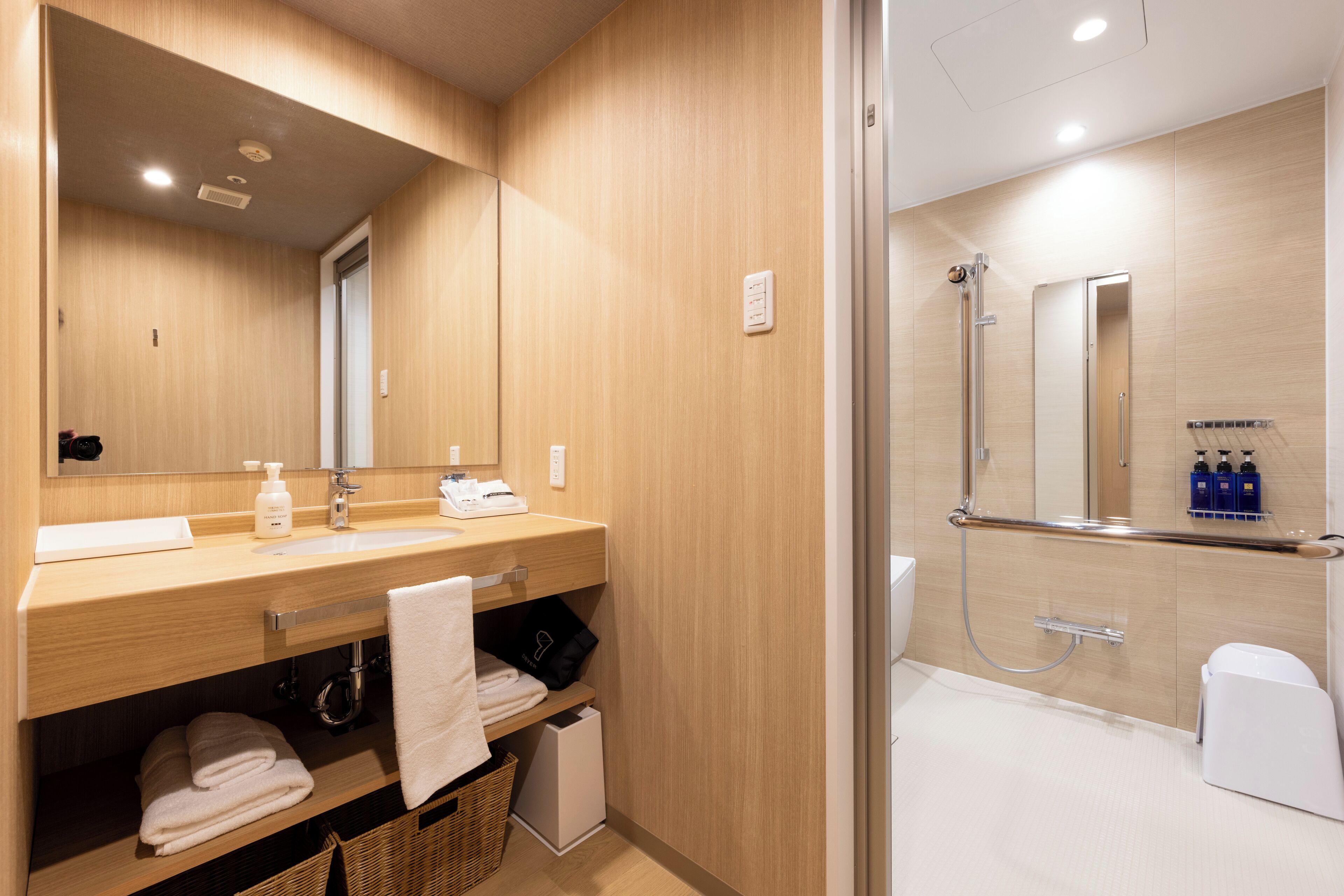 A modern bathroom with a wooden vanity, a large mirror, a shower area, and a white toilet.