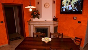 Une salle à manger avec une table en bois, des chaises, une cheminée et un téléviseur fixé au mur.