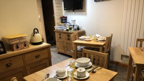 Una cocina acogedora con armarios de madera, una mesa de comedor preparada para cuatro personas y un televisor montado en la pared.