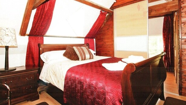 Un dormitorio con cama de madera, cortinas rojas, cómoda de madera y ventana con vistas.