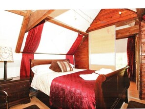 A bedroom with a wooden bed, red curtains, a wooden dresser, and a window with a view.
