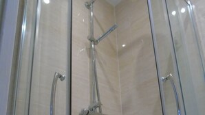 Ducha con cerramiento de vidrio, cabezal de ducha manual y ducha de lluvia fija.