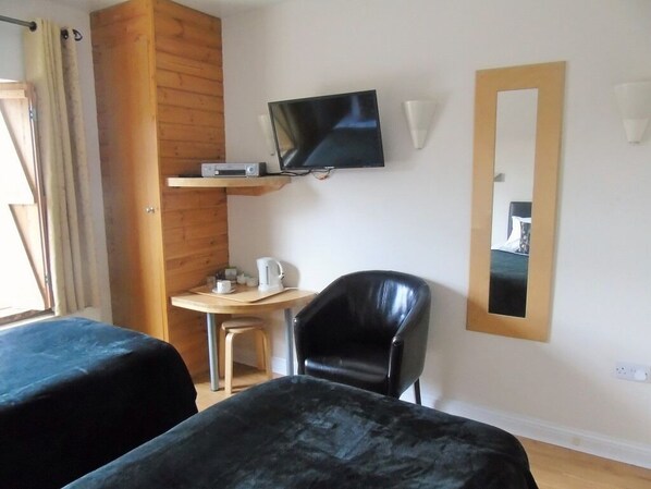 A hotel room with two beds, a TV, a small table with a kettle, a chair, and a mirror on the wall.