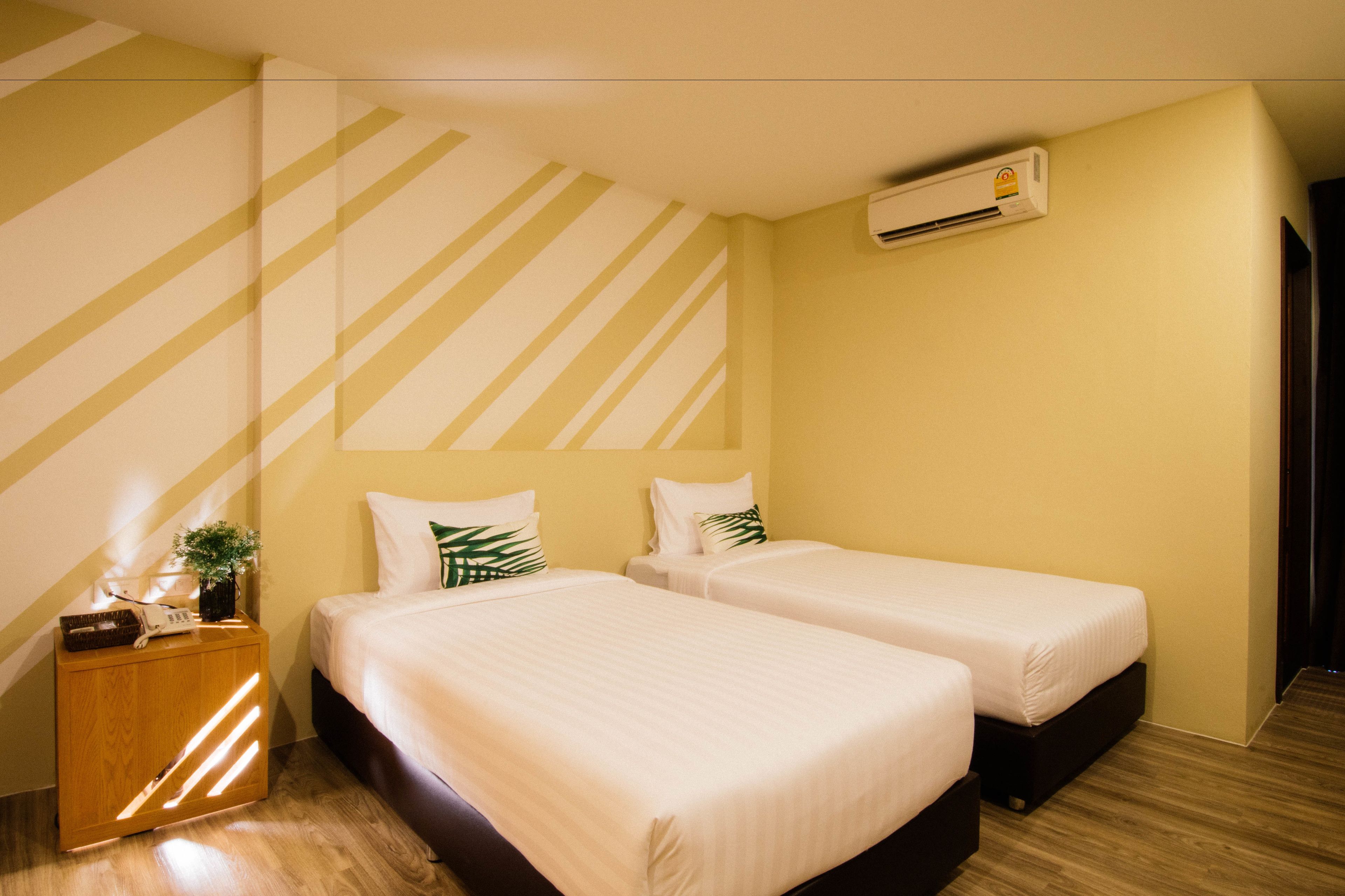 A hotel room with two beds, a wooden nightstand, and an air conditioning unit on the wall.