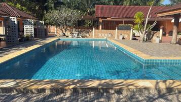 A rectangular swimming pool with blue tiles, surrounded by a wooden deck and shaded by trees.