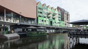 A riverside hotel with a green facade, outdoor seating, and a bridge connecting to the building. - easyHotel Amsterdam Zaandam (Zaandam)