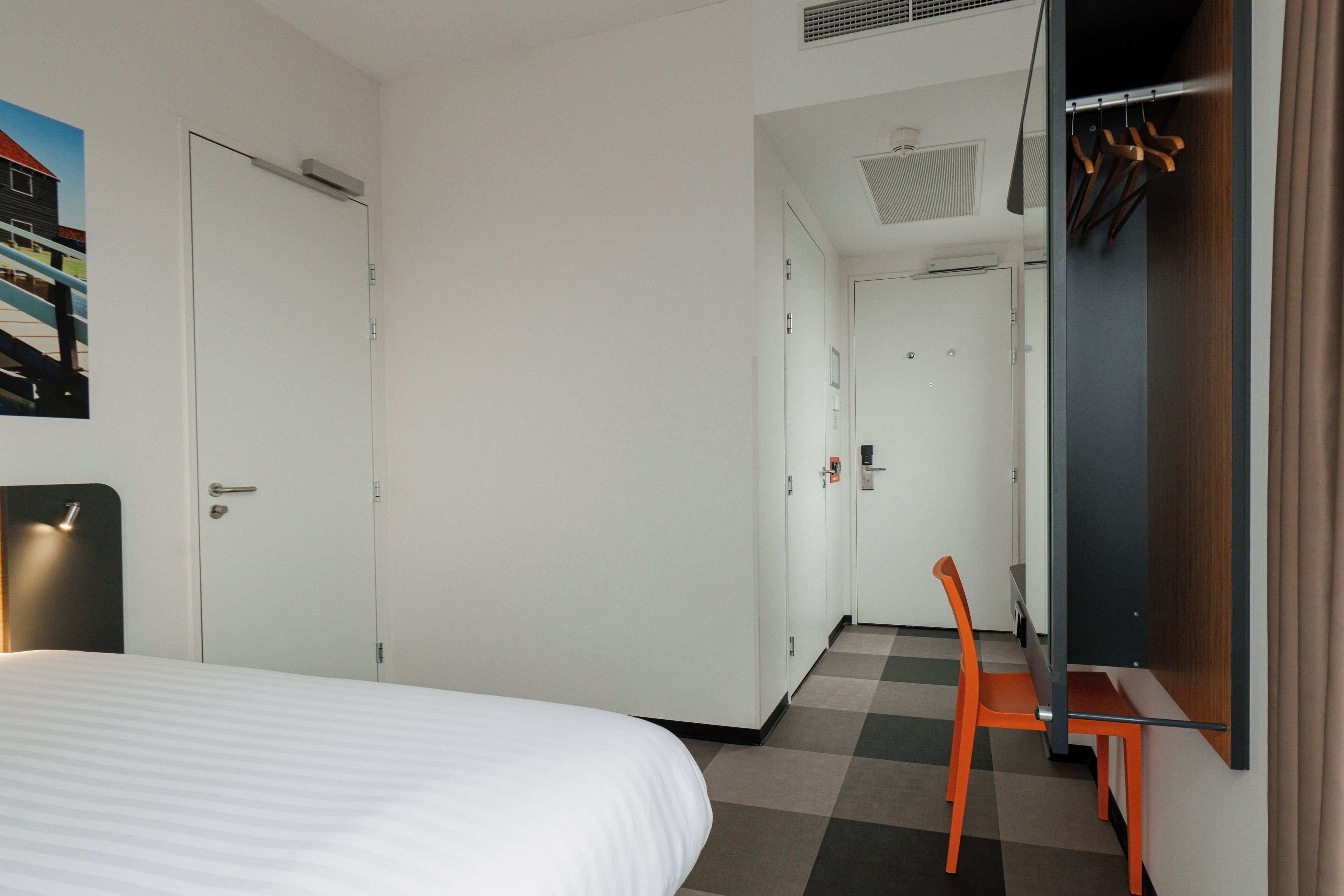 A hotel room with a bed, a desk, a chair, and a wardrobe.