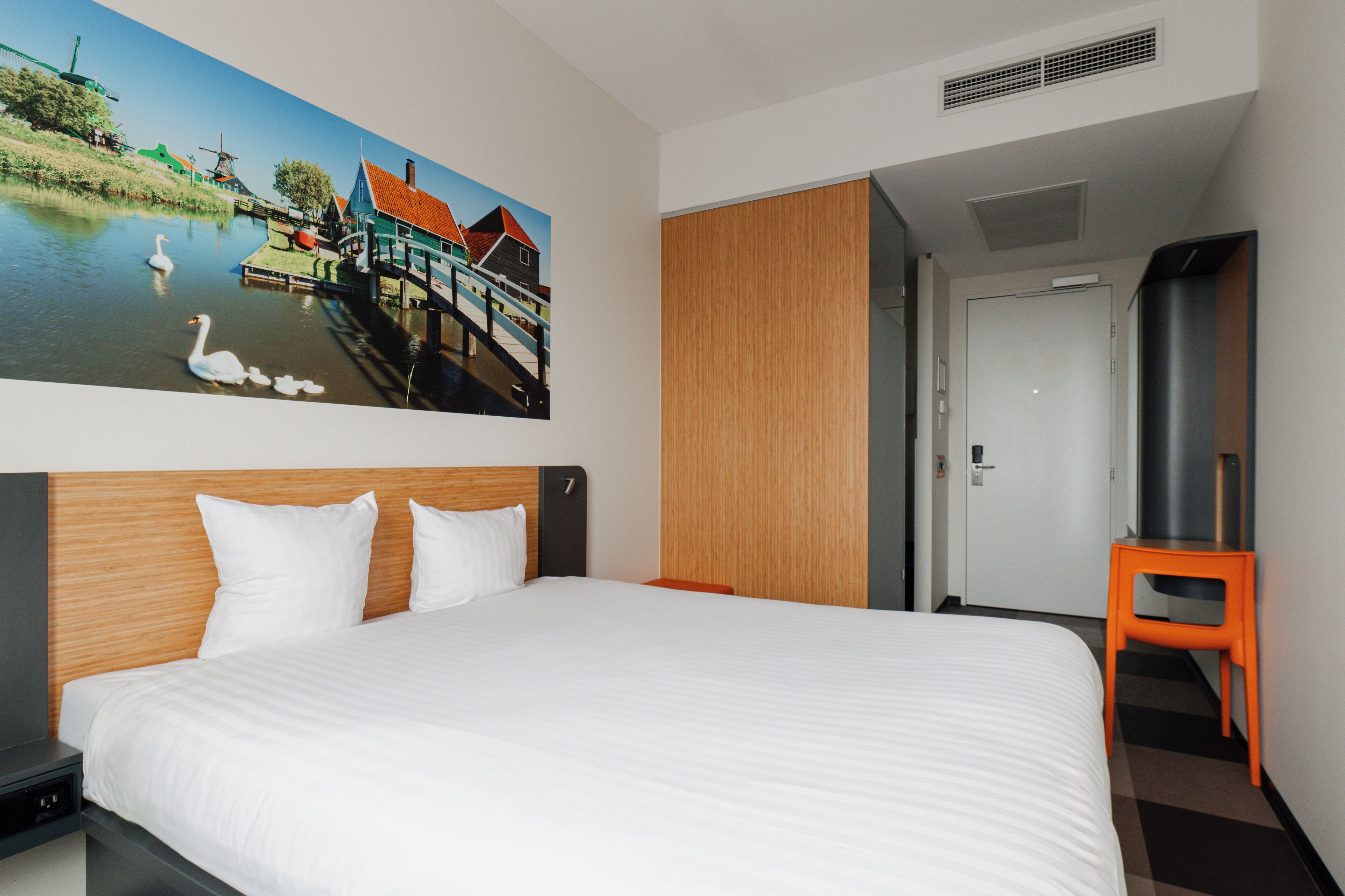 Habitación de hotel con una cama grande, cabecera de madera, un cuadro con vista a un canal, televisor y un armario.