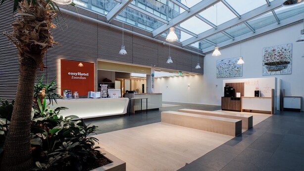 A spacious hotel lobby with a reception desk, modern furnishings, and a large glass ceiling allowing natural light. - easyHotel Amsterdam Zaandam (Zaandam)