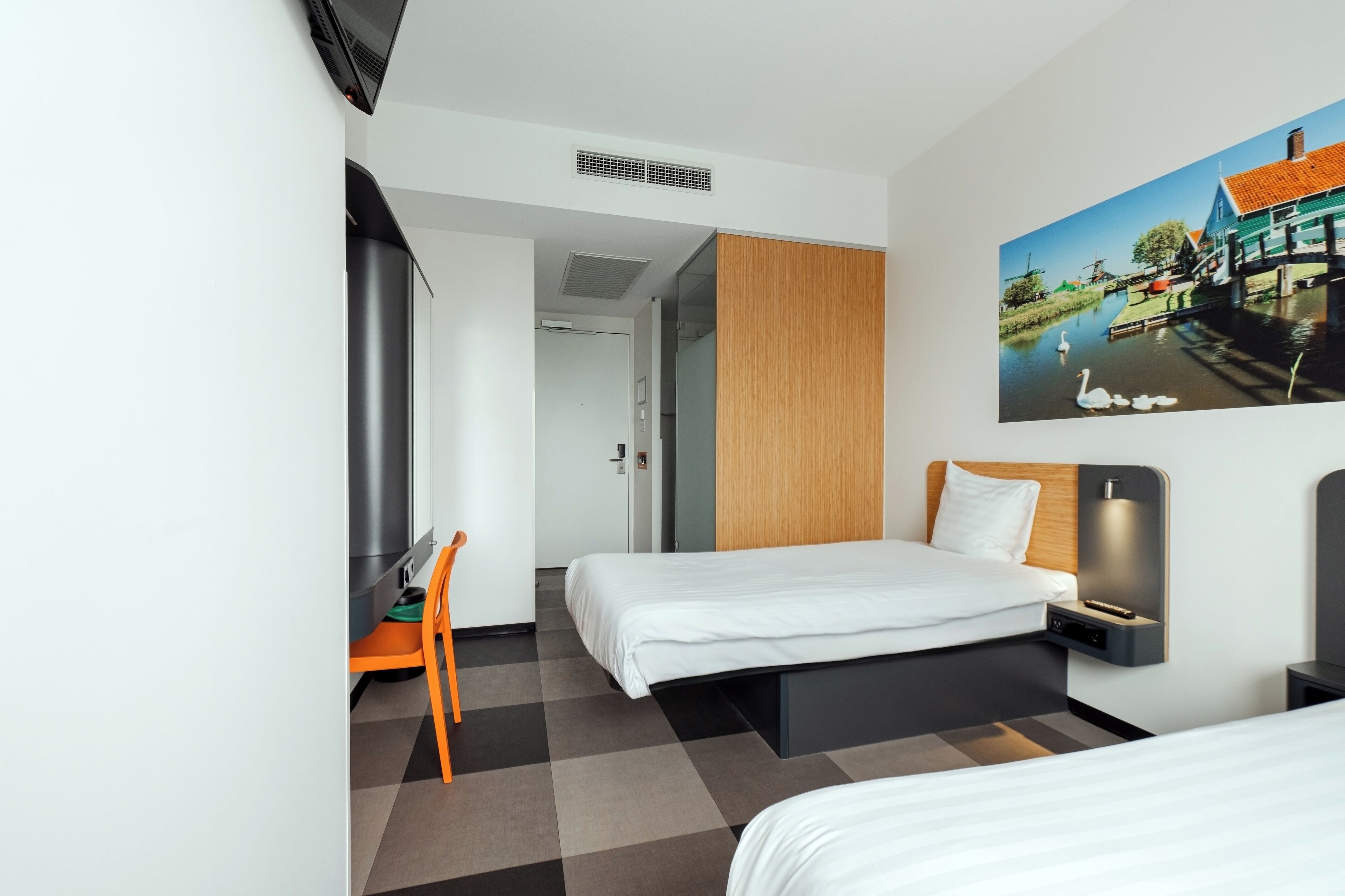 A modern hotel room with two beds, a desk, and a painting of a canal scene.